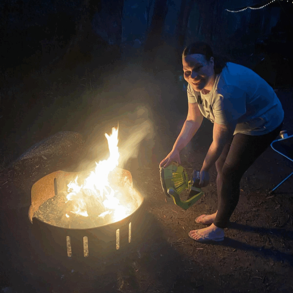 woman stoking fire with portable fan while camping